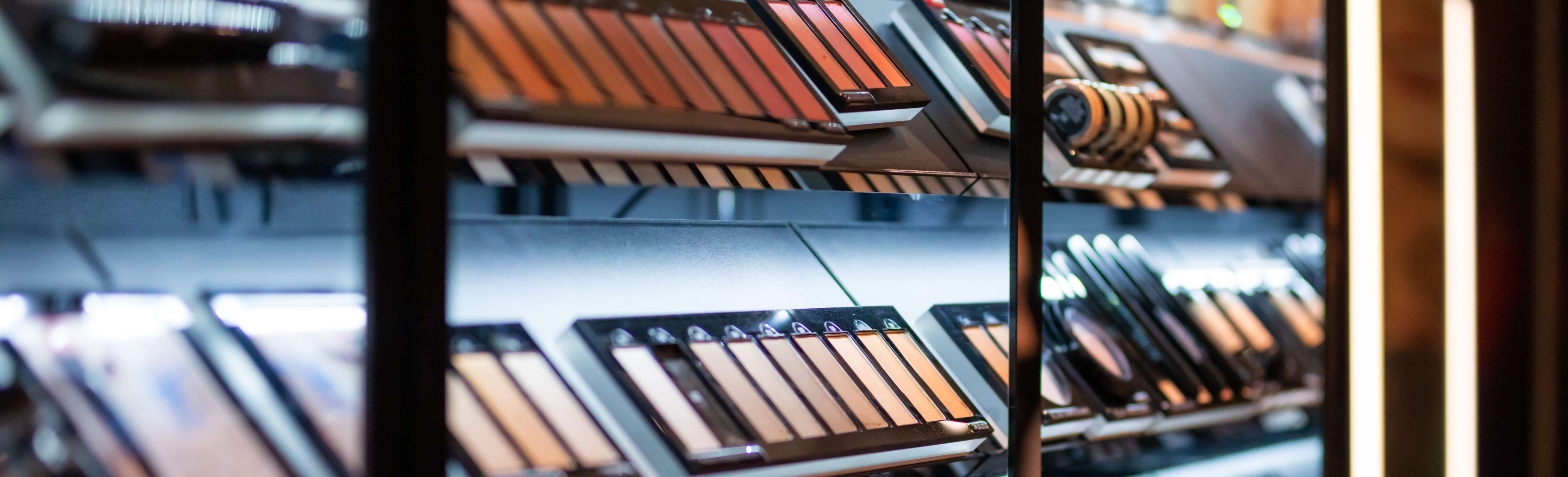 A makeup shelf within a supermarket displaying various foundation options behind glass casing with black accents.