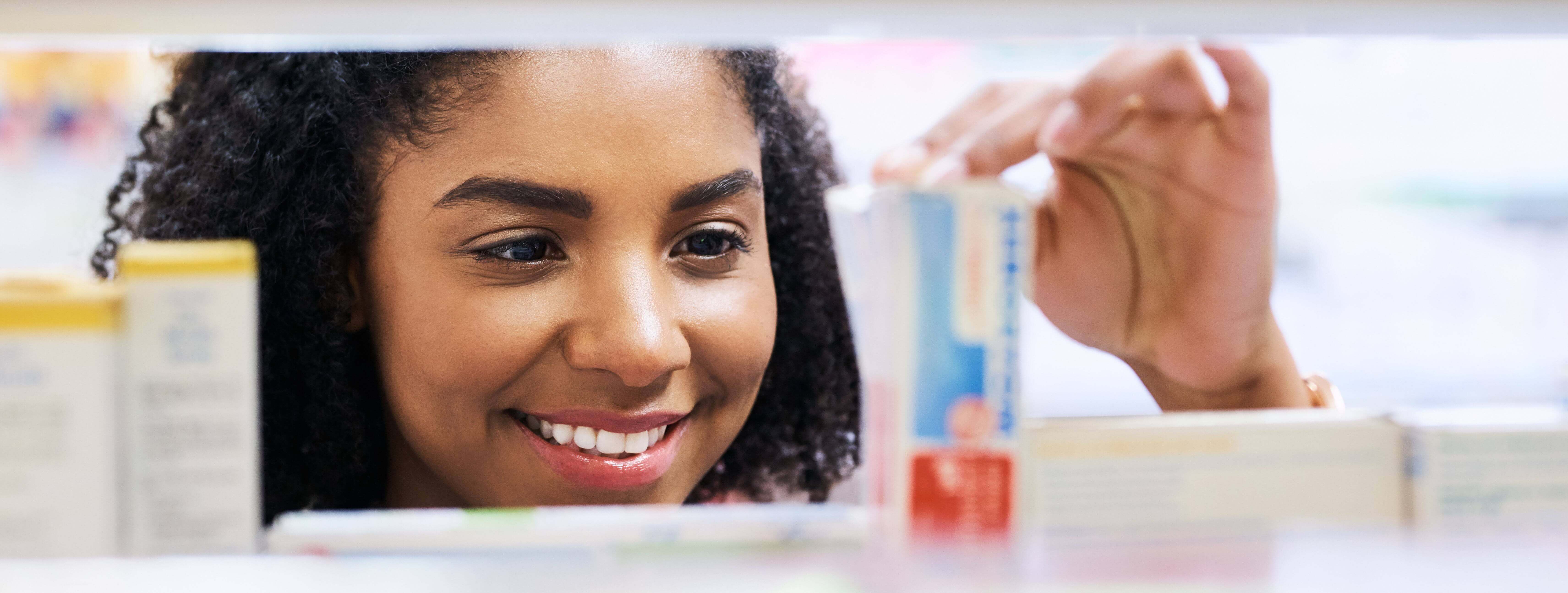 A woman with curly hair is smiling as she reads the description written on the box of a beauty product.